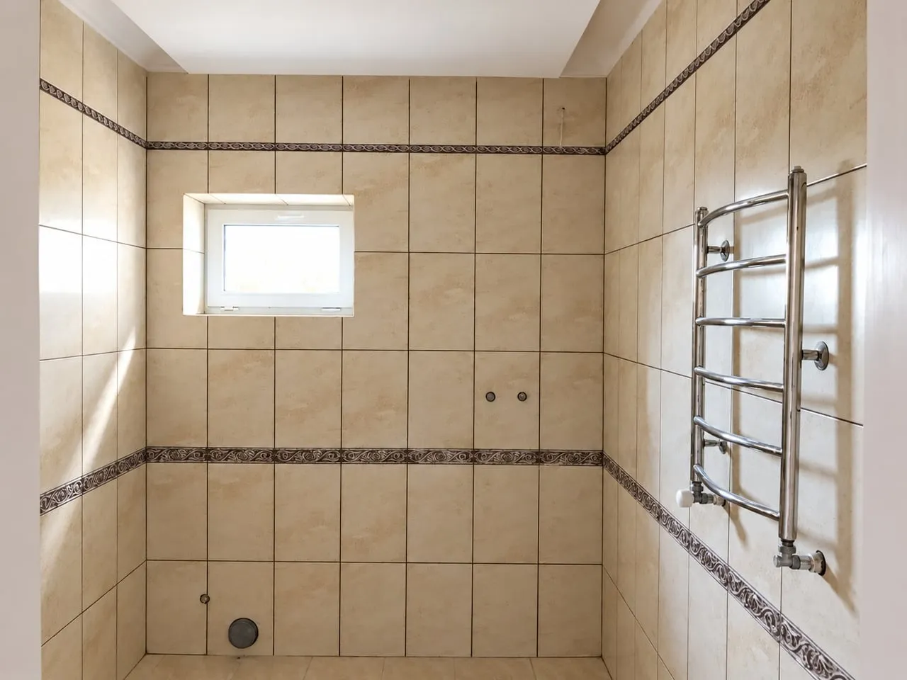 Salle de bain carrelée : faïence beige, frises décoratives, petite fenêtre et sèche-serviettes