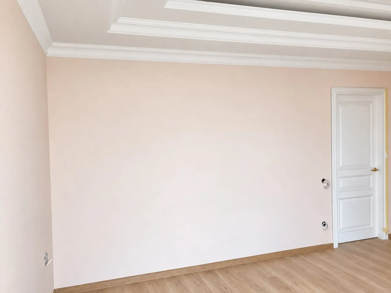 Mur peint rose pâle avec corniche blanche et porte intérieure